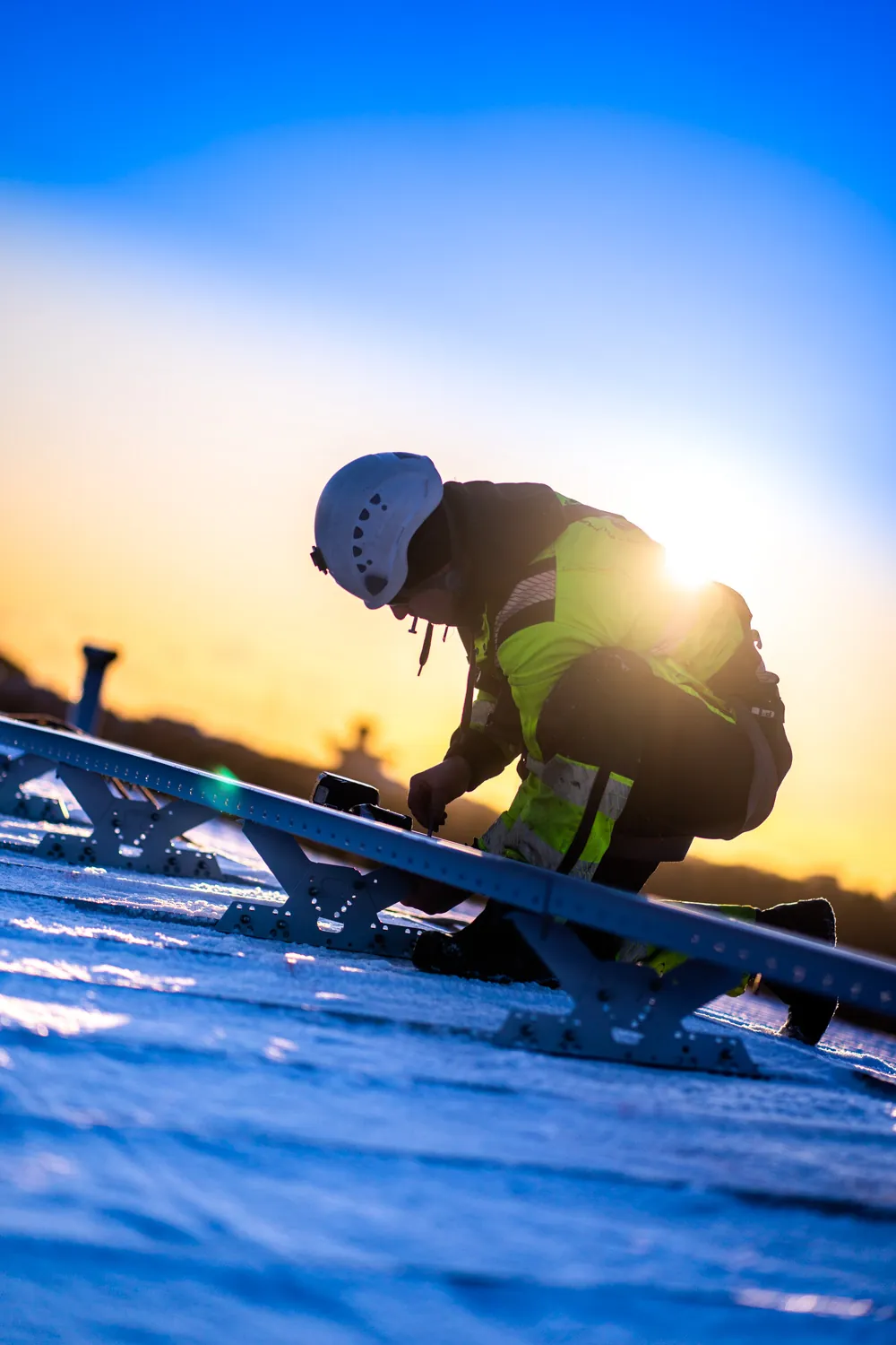 Asentaja asentaa kattosiltaa lumisella katolla auringonnousussa
