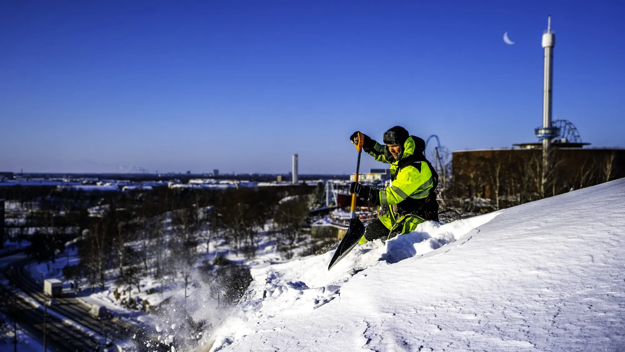 Kattoasentaja pudottaa lunta katolta turvavaljaisiin kiinnitettynä