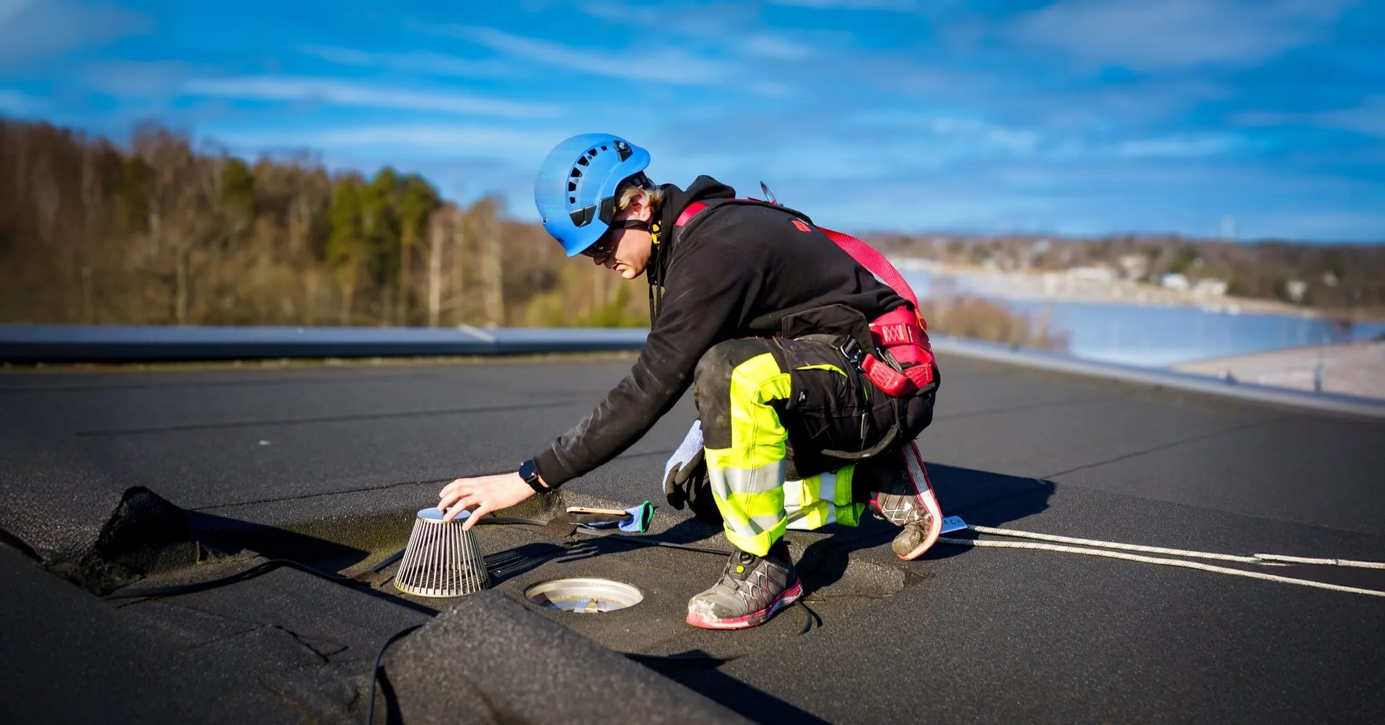 Kattohuoltoasentaja puhdistaa kattokaivon sihtiä bitumikatolla